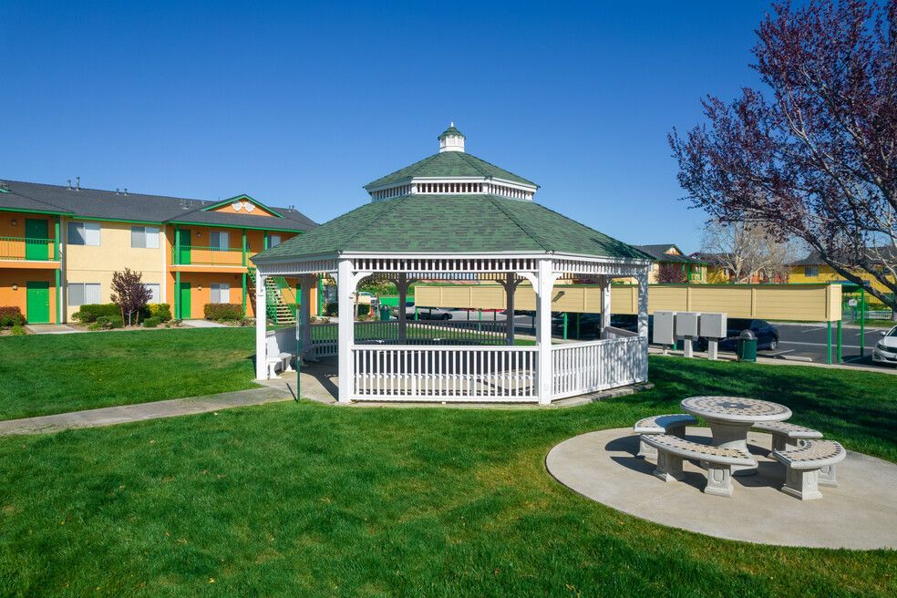 A gazebo with a green roof sits in the middle of a lush green park.