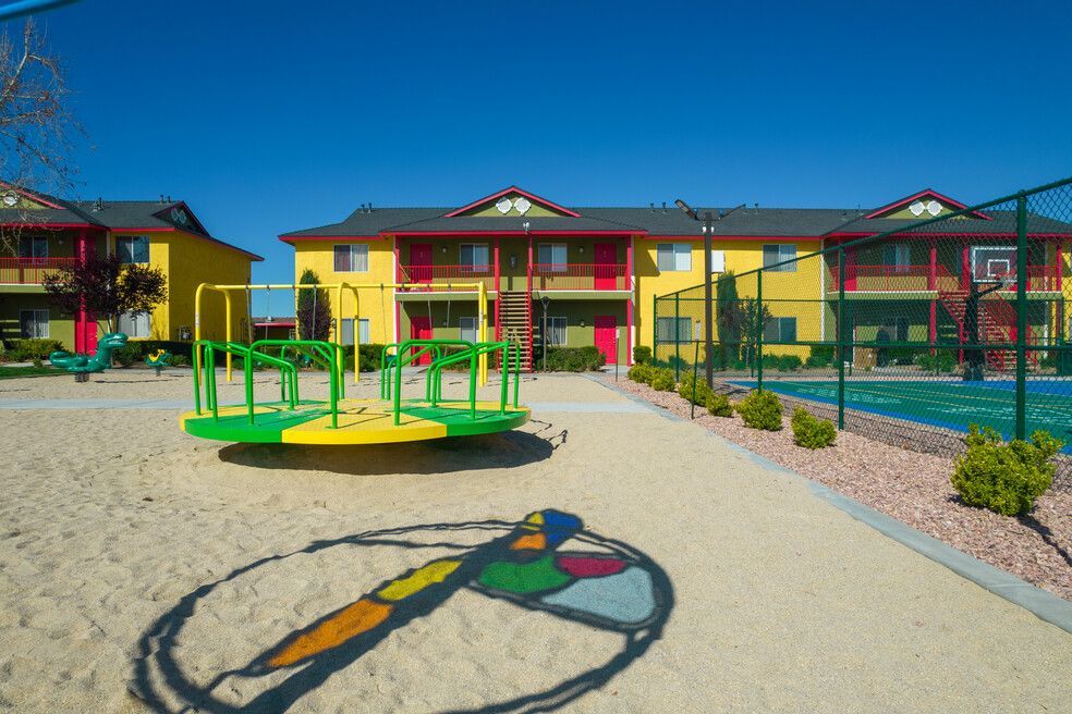 A playground with a merry go round and a basketball court in front of a building.