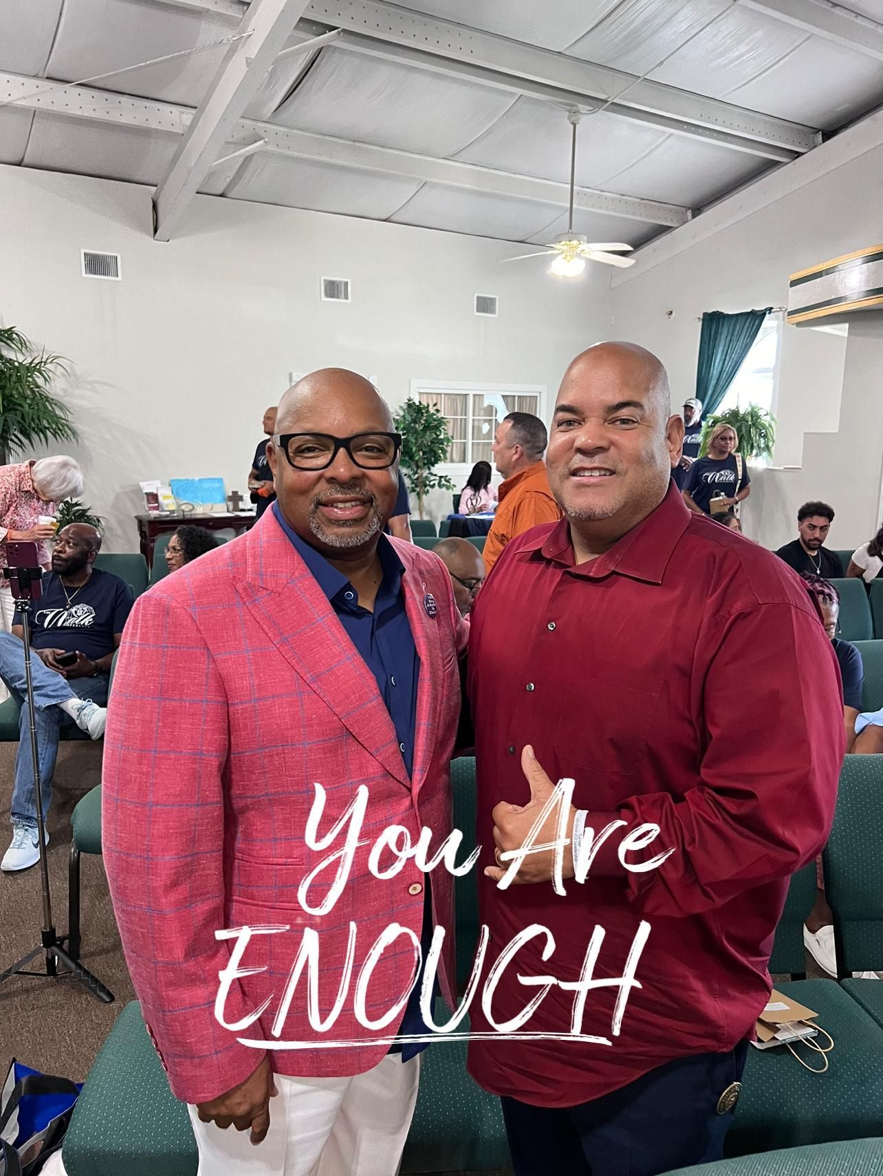 Two men are standing next to each other in a room with a sign that says `` you are enough ''.