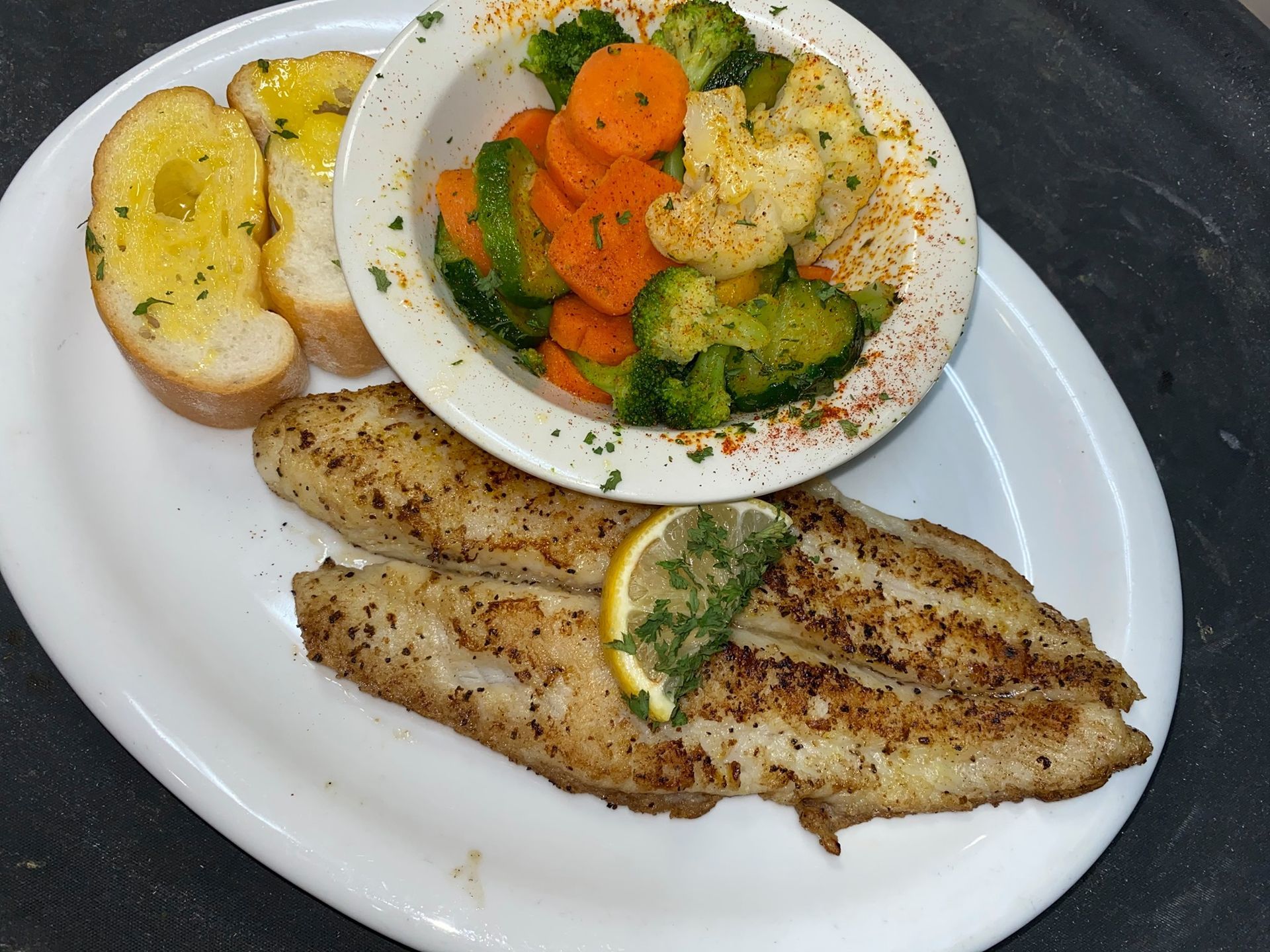 A white plate topped with fish , vegetables and garlic bread.