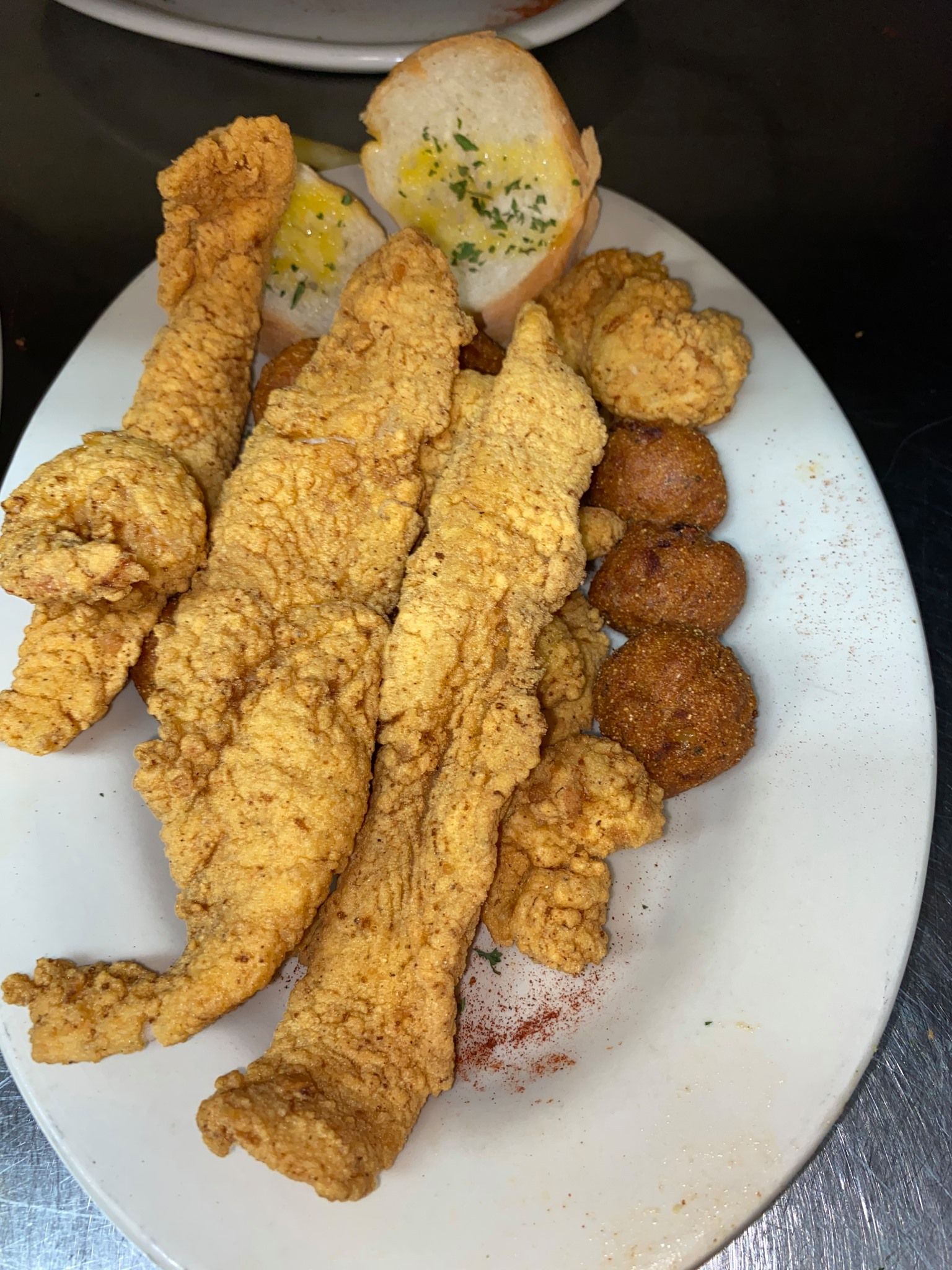A white plate topped with fried fish and bread on a table.
