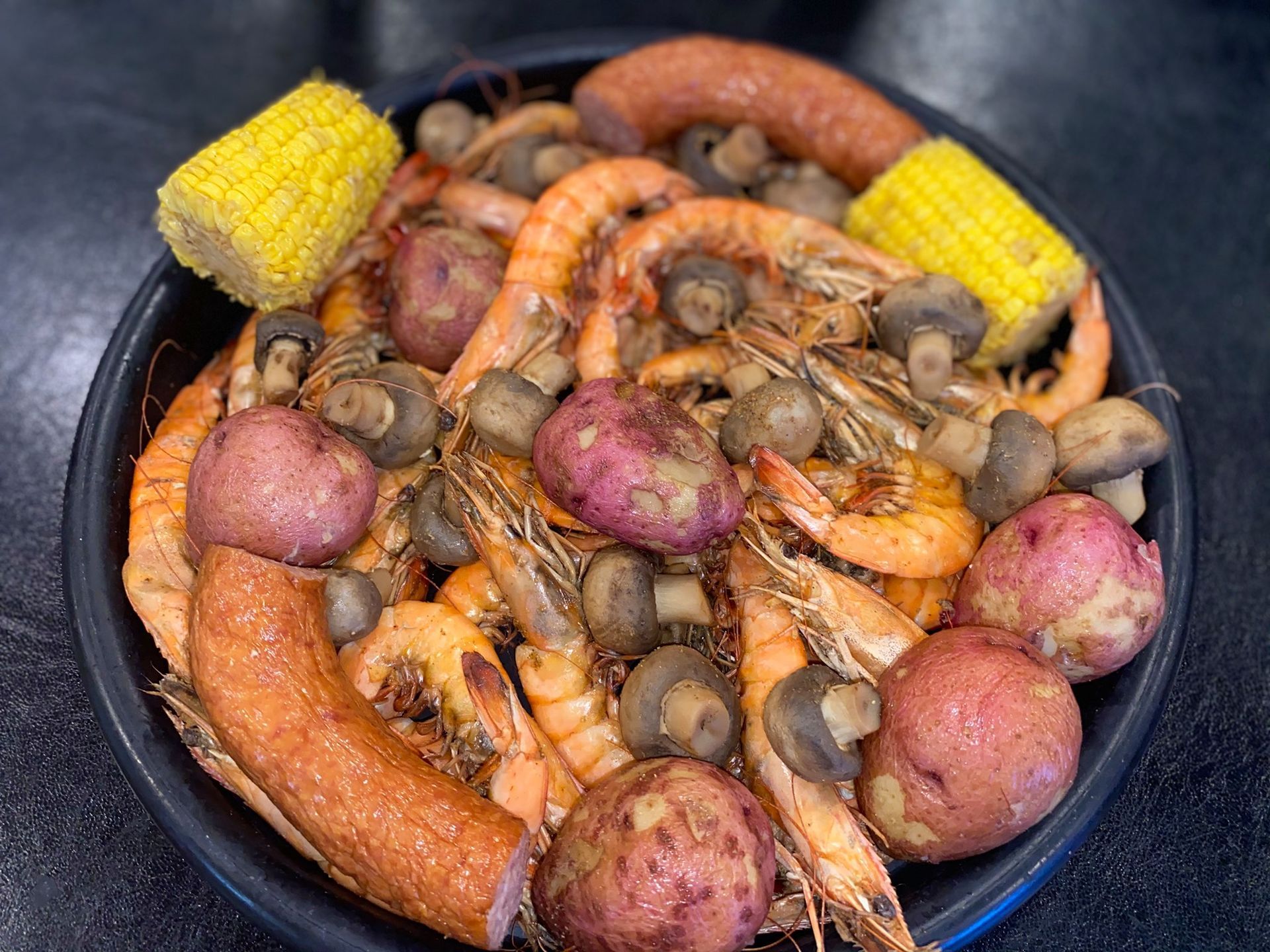 A plate of food with shrimp , potatoes , corn on the cob and sausage.