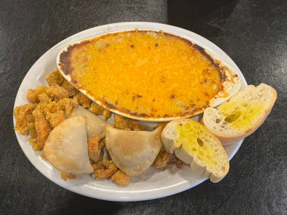 A white plate topped with a casserole , shrimp , bread and garlic bread.