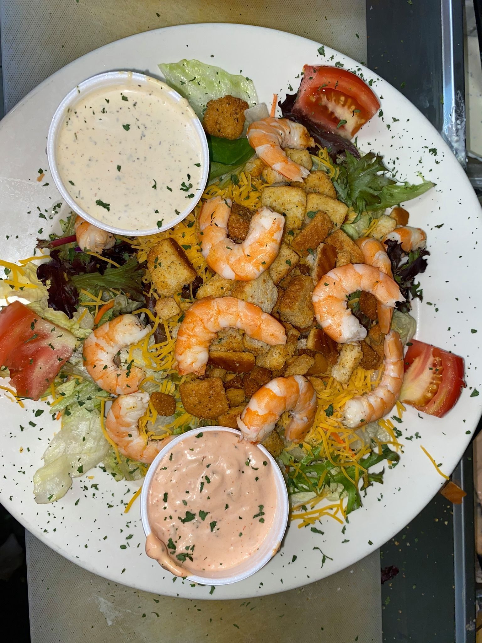 A salad with shrimp , croutons , cheese and tomatoes on a white plate.