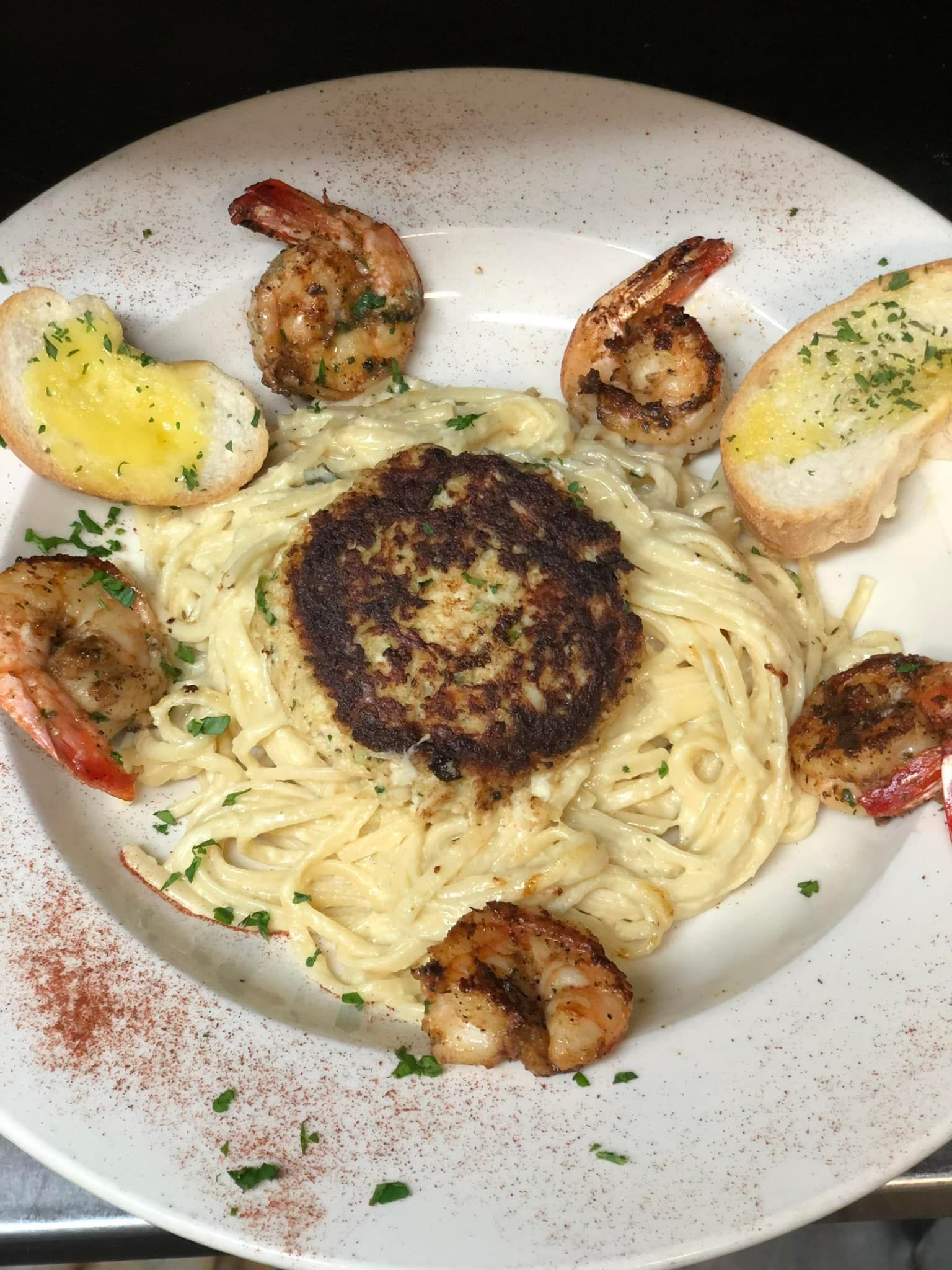 A white plate topped with spaghetti , shrimp , crab cakes and garlic bread.