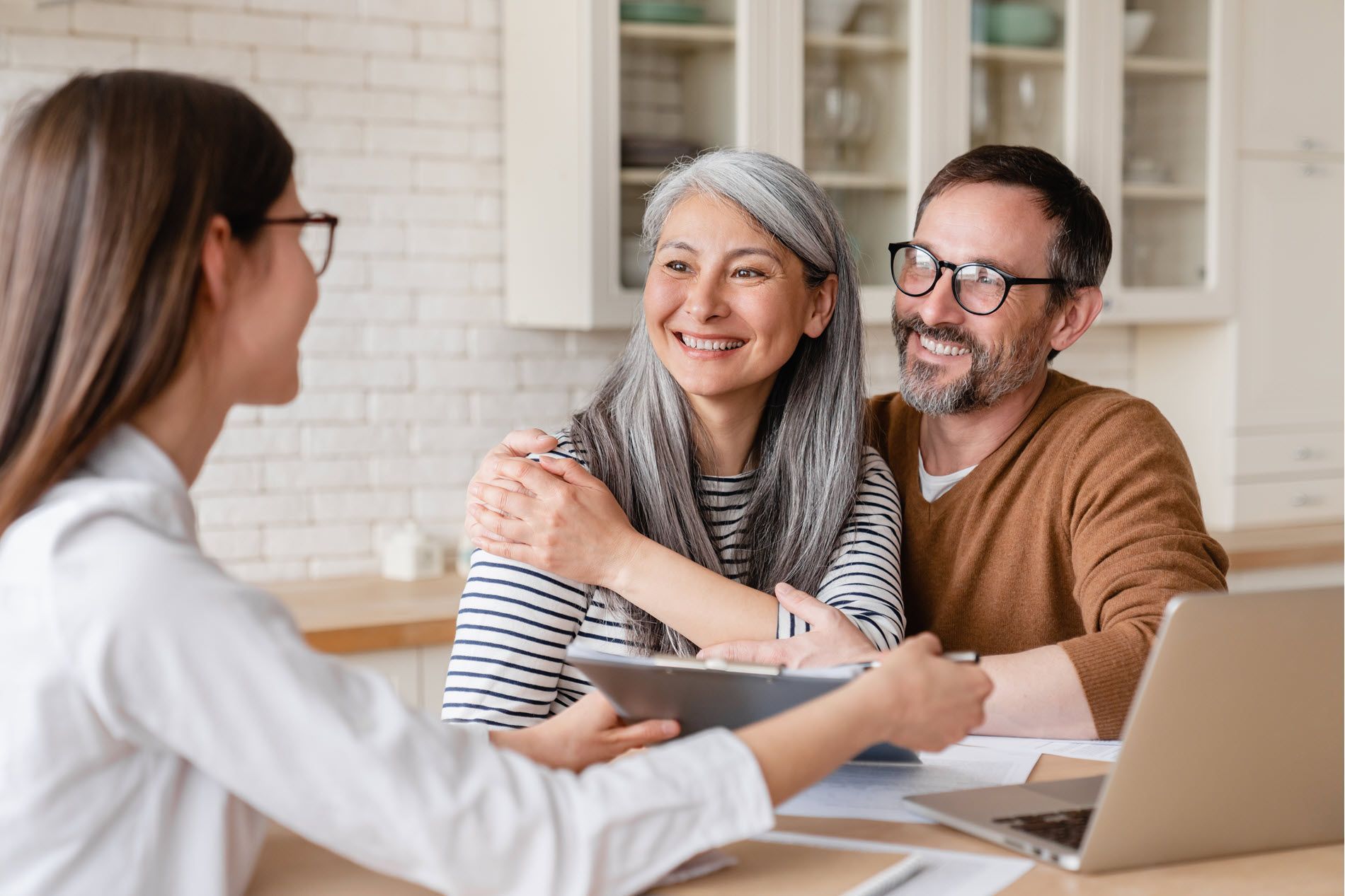 Woman meeting with a smiling couple at a table, discussing documents beside a laptop.