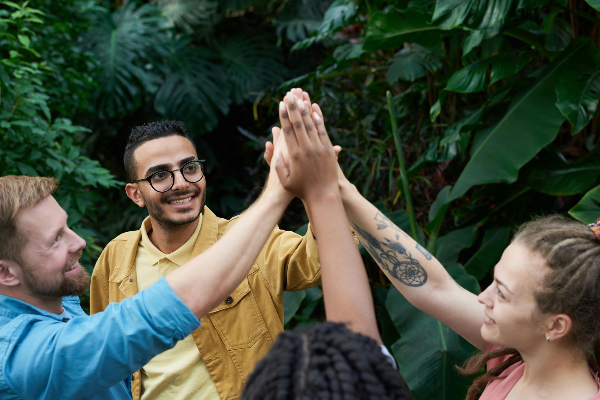 Group of people high-fiving in a lush green garden, smiling and celebrating together