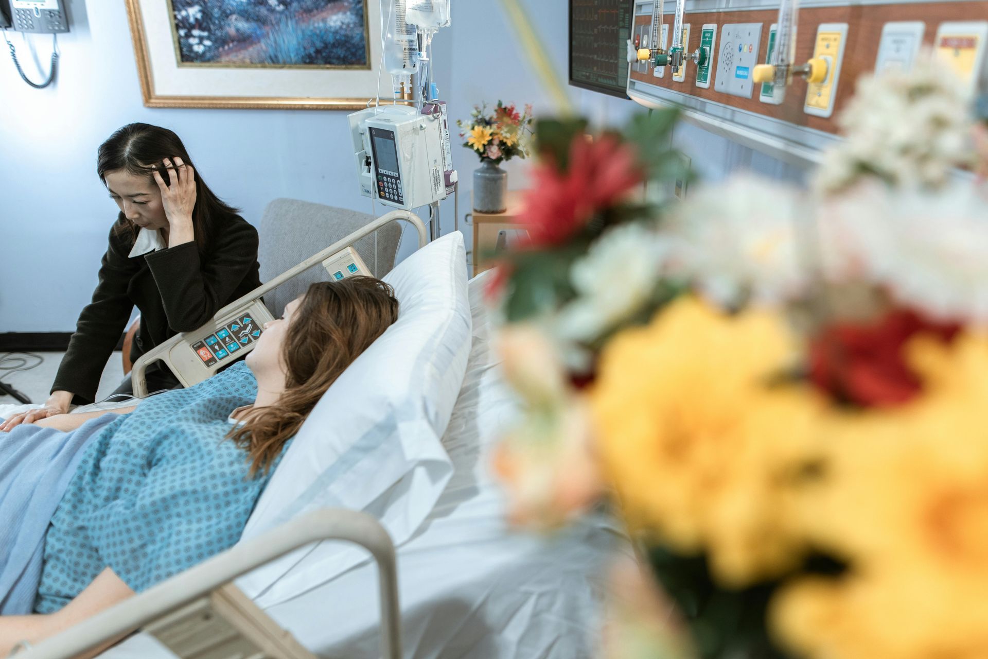 Hospital room with a patient in bed and a worried visitor sitting beside them