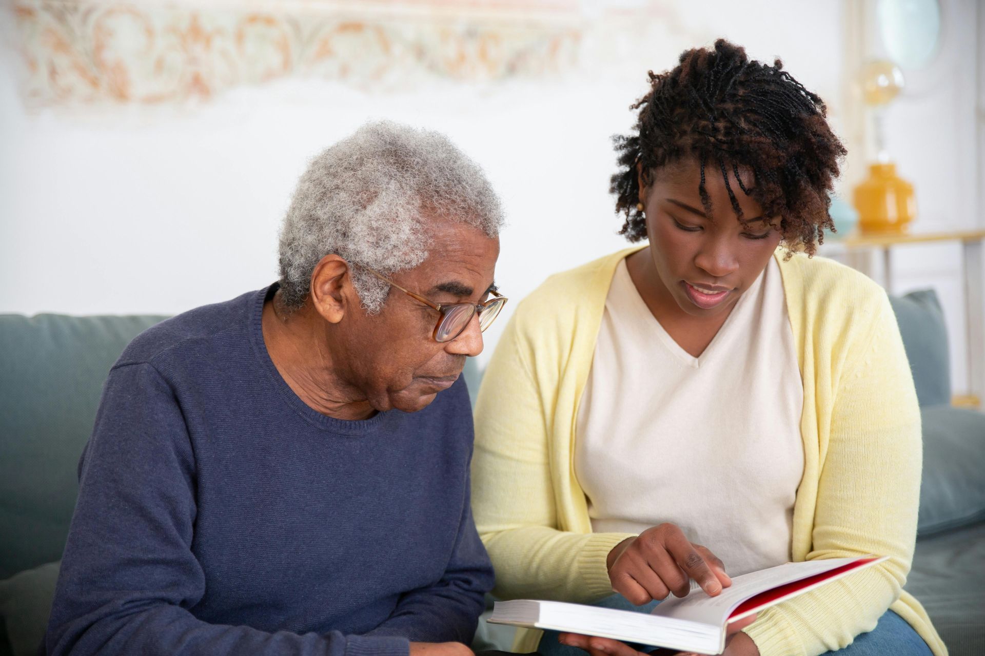 Two people sit on a couch reading an open book together