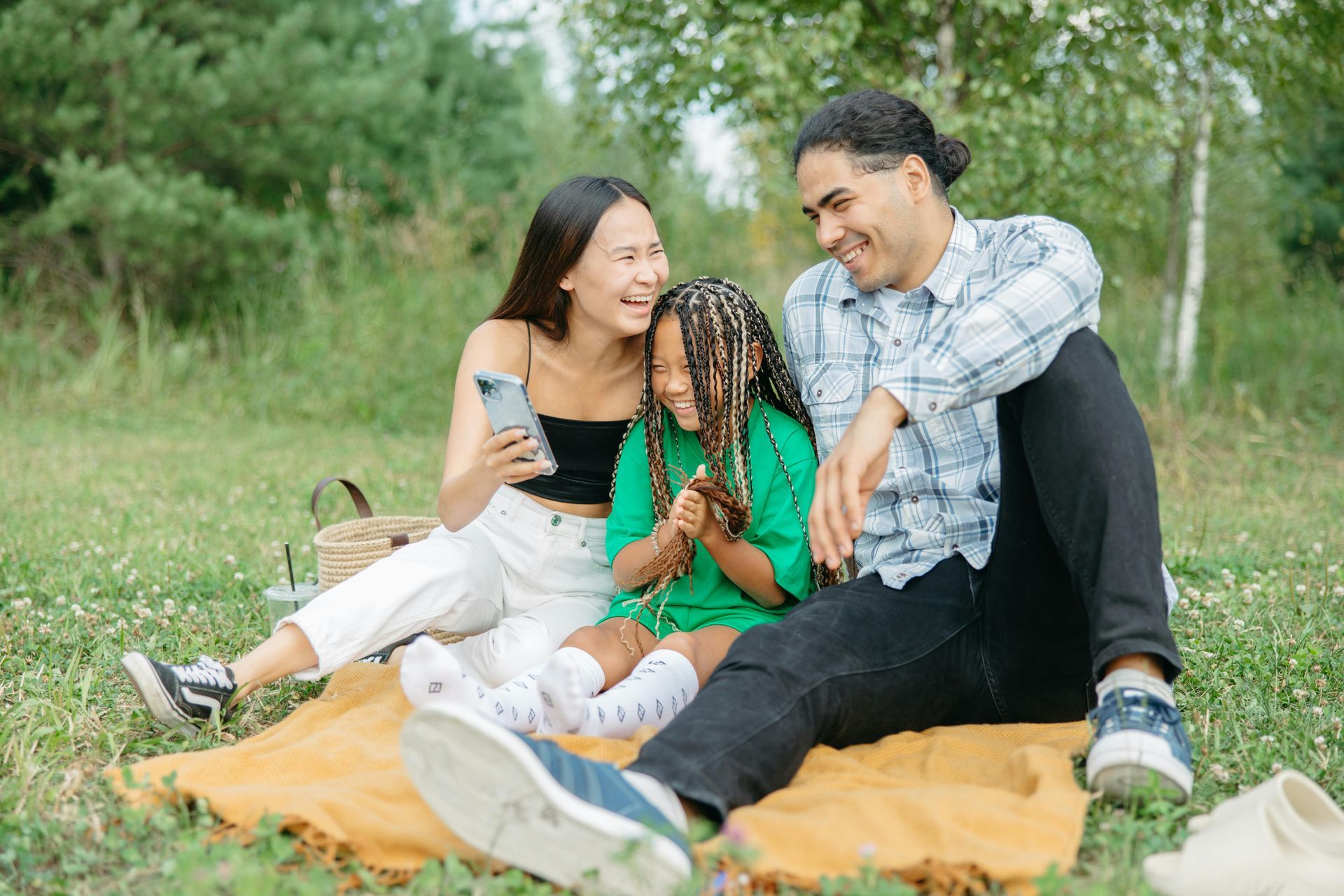 Family sitting on a blanket in a grassy park, smiling and looking at each other.