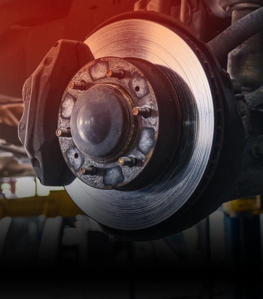 Car brake disc and caliper, close-up. Metallic silver and black components. Reddish lighting | NOR-CAL AUTOMOTIVE