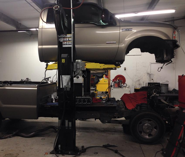 Tan pickup truck raised on a lift in a garage, undergoing repair. The front bumper is missing | NOR-CAL AUTOMOTIVE