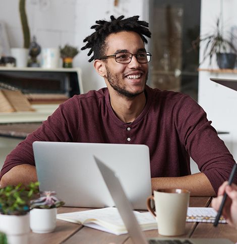 A man is sitting at a table with a laptop and a cup of coffee.