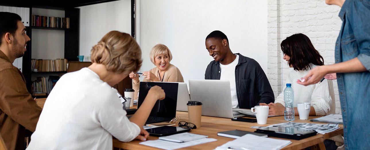 A group of people are sitting around a table with laptops.