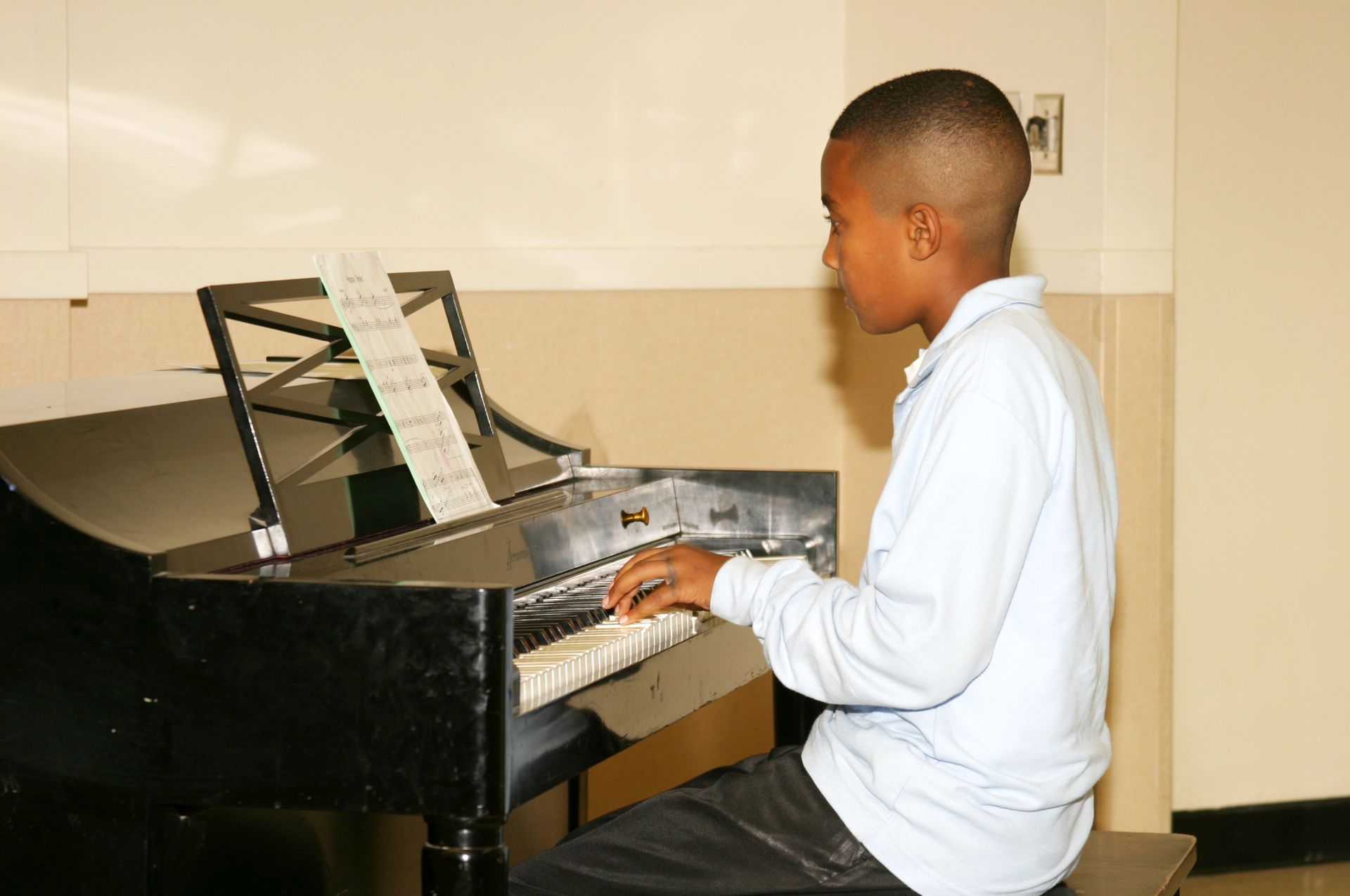 A young boy is sitting on a bench playing a piano.