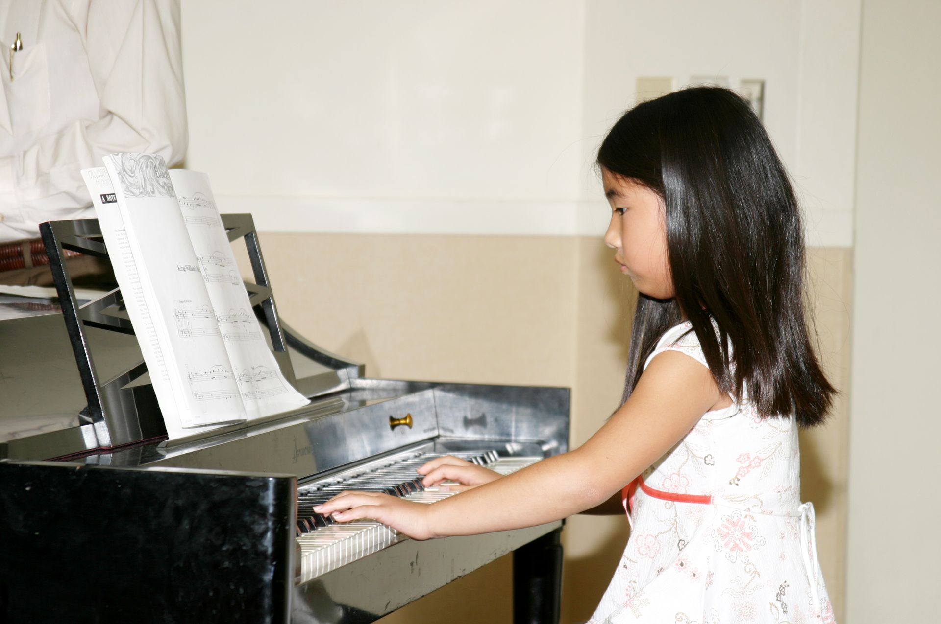 A young girl in a white dress is playing a piano.