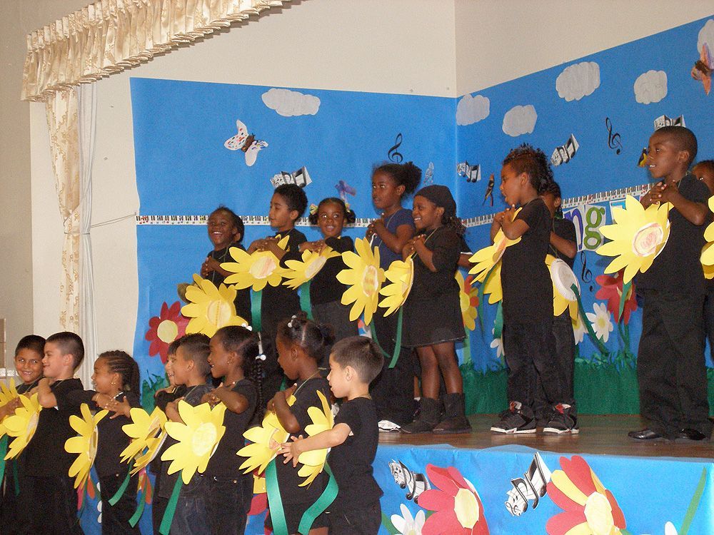 A group of children are standing on a stage wearing sunflowers.