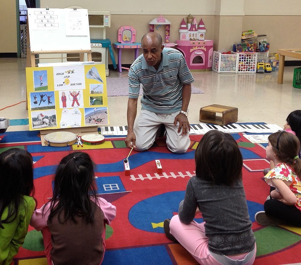 A man is kneeling down in front of a group of children.