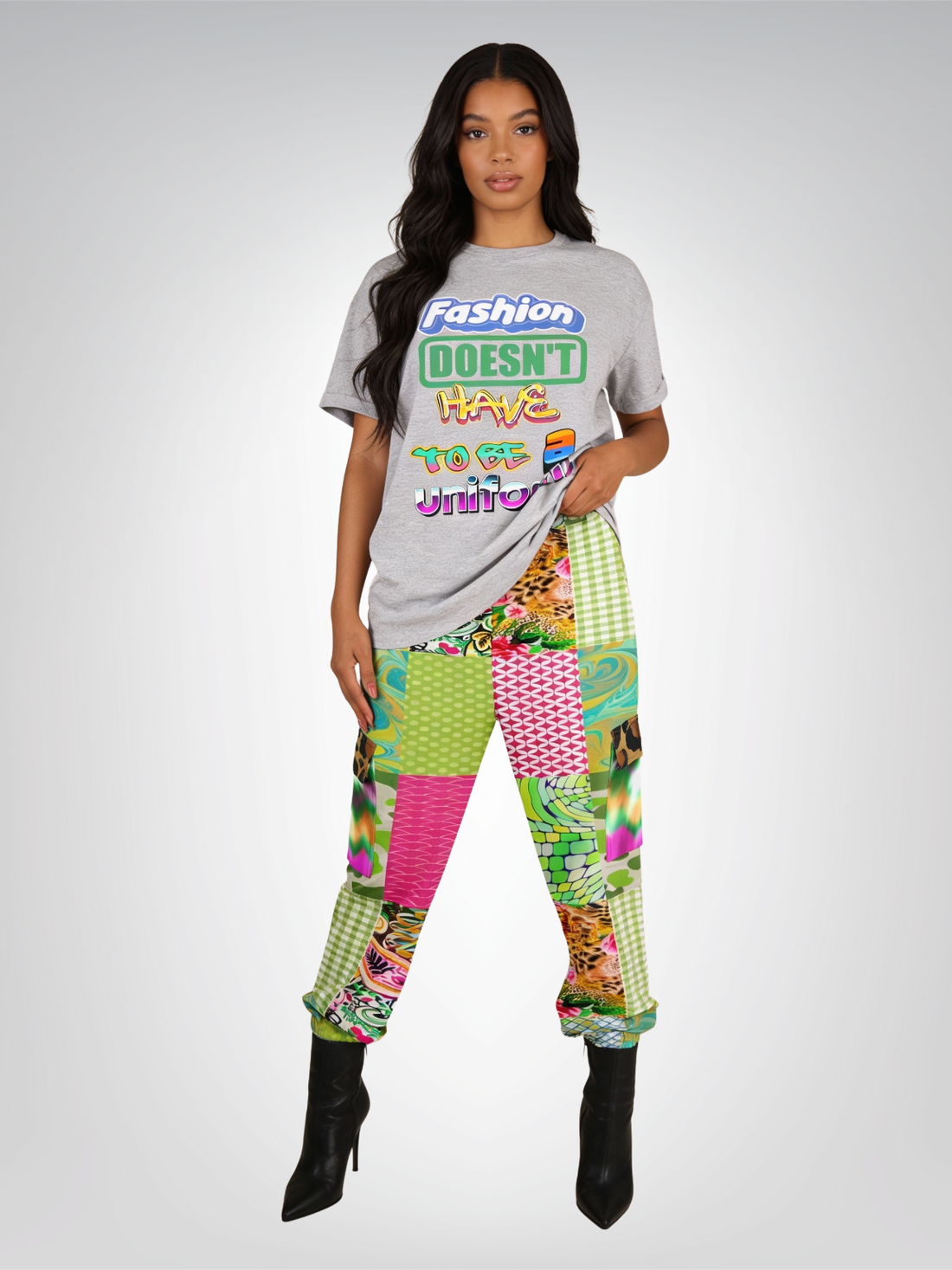 Woman in gray tee with slogan, patchwork pants, and black boots.
