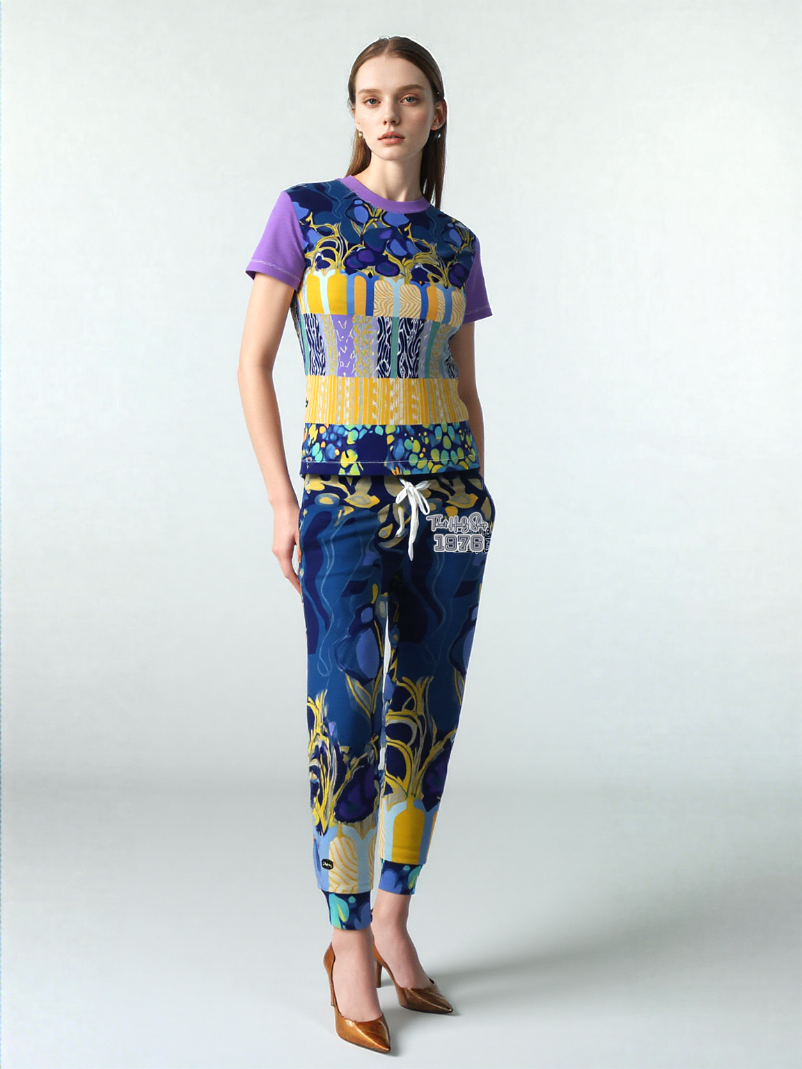 Woman wearing a blue floral patterned top and pants, with purple sleeves, and tan heels.