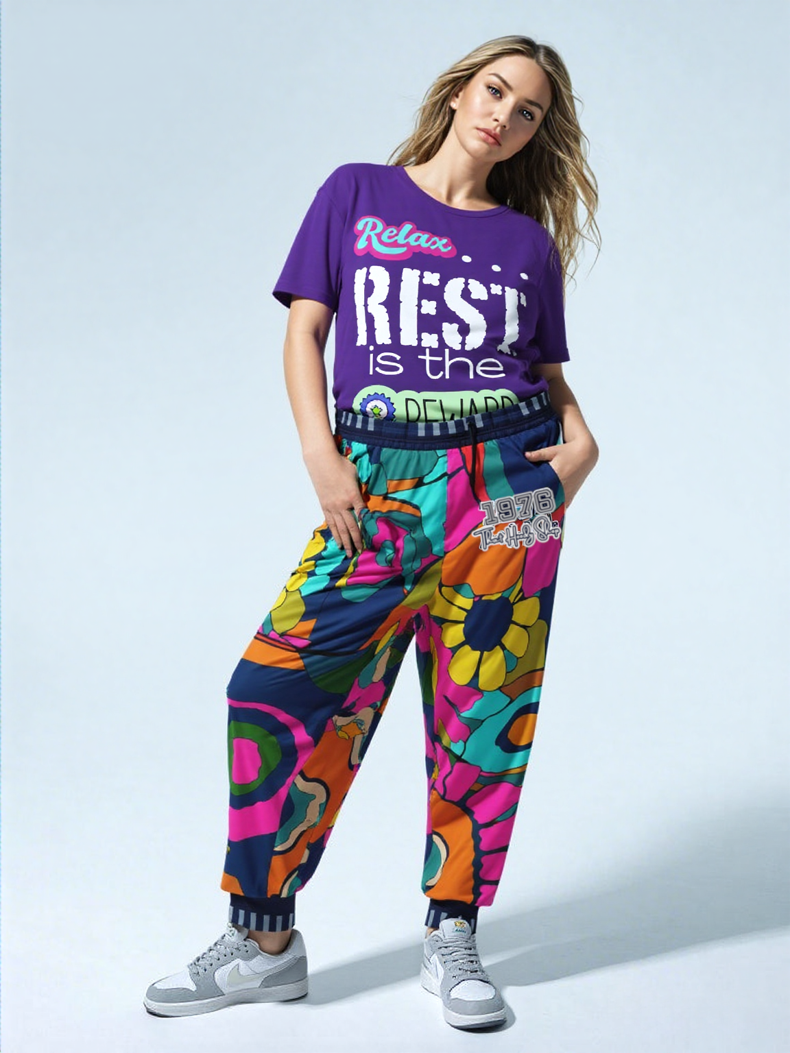 Woman in purple tee and patterned pants, relaxed pose, gray sneakers. Studio setting.