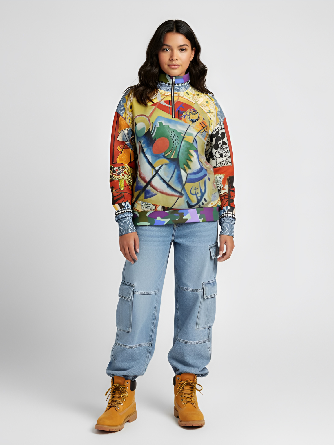 Woman wearing a colorful abstract sweatshirt, light blue cargo jeans, and tan boots, standing.