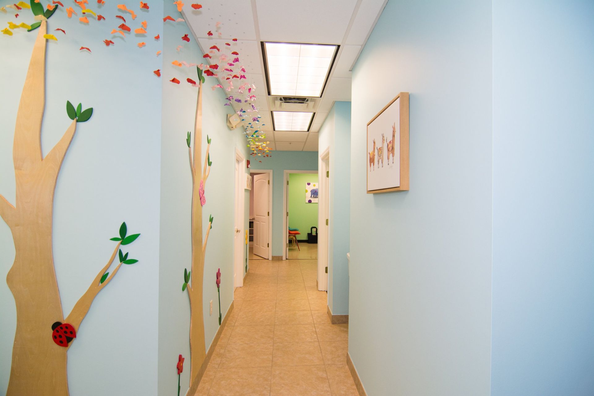 photo of the hallway showing 4 white doors, light blue walls with tree decals on the left and  a picture frame handing on the right wall.
