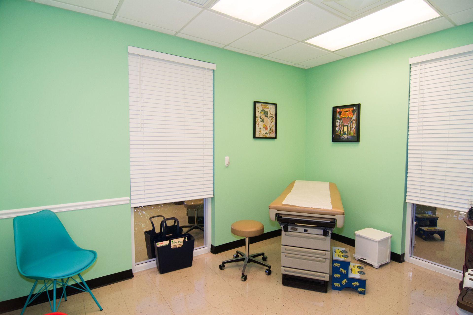 consultation room, one examination bed in the corner between two windows with blinds and a blue chair on the farther left