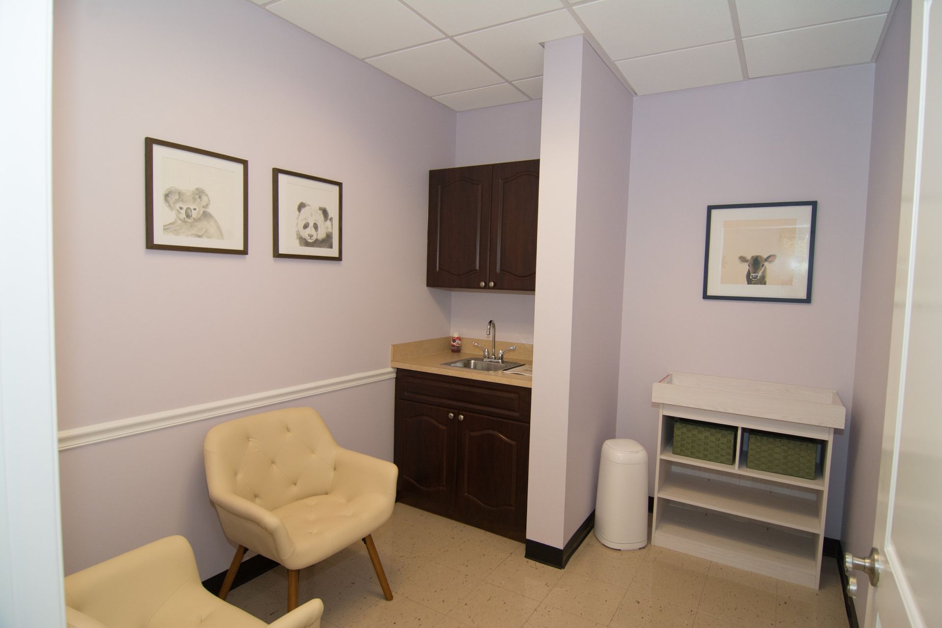 Photo of their waiting room with tow beige colored chairs beside the sink, two pencil drawn painting on the wall behind the chair and a table top right beside the door on the right