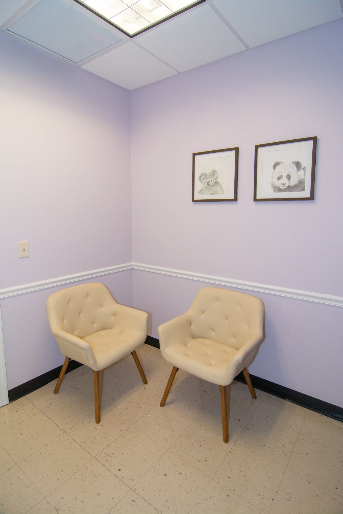 two beige colored chairs against the wall, light purple background and two framed pencil drawings of a koala and panda hanging on the wall.