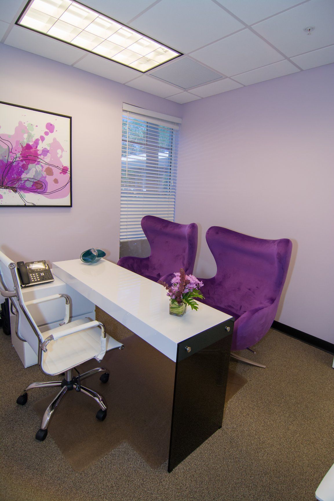 Photo inside the consultation office. White table, white swivel chair for the doctor and two purple for the patients