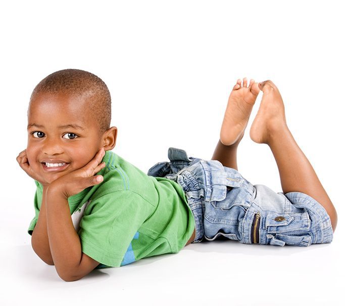 cute black toddler wearing a green shirt smiling, laying on his belly with his chin on both hands
