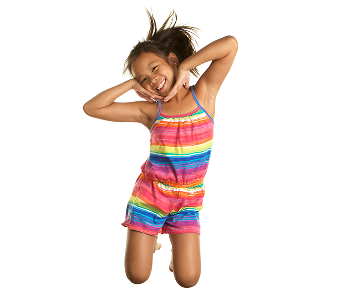 Young girl wearing a rainbow colored tank top and shorts jumping with excitement