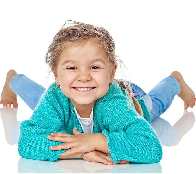 Cute white girl toddler wearing a bright blue cardigan and jeans lying on her belly smiling 