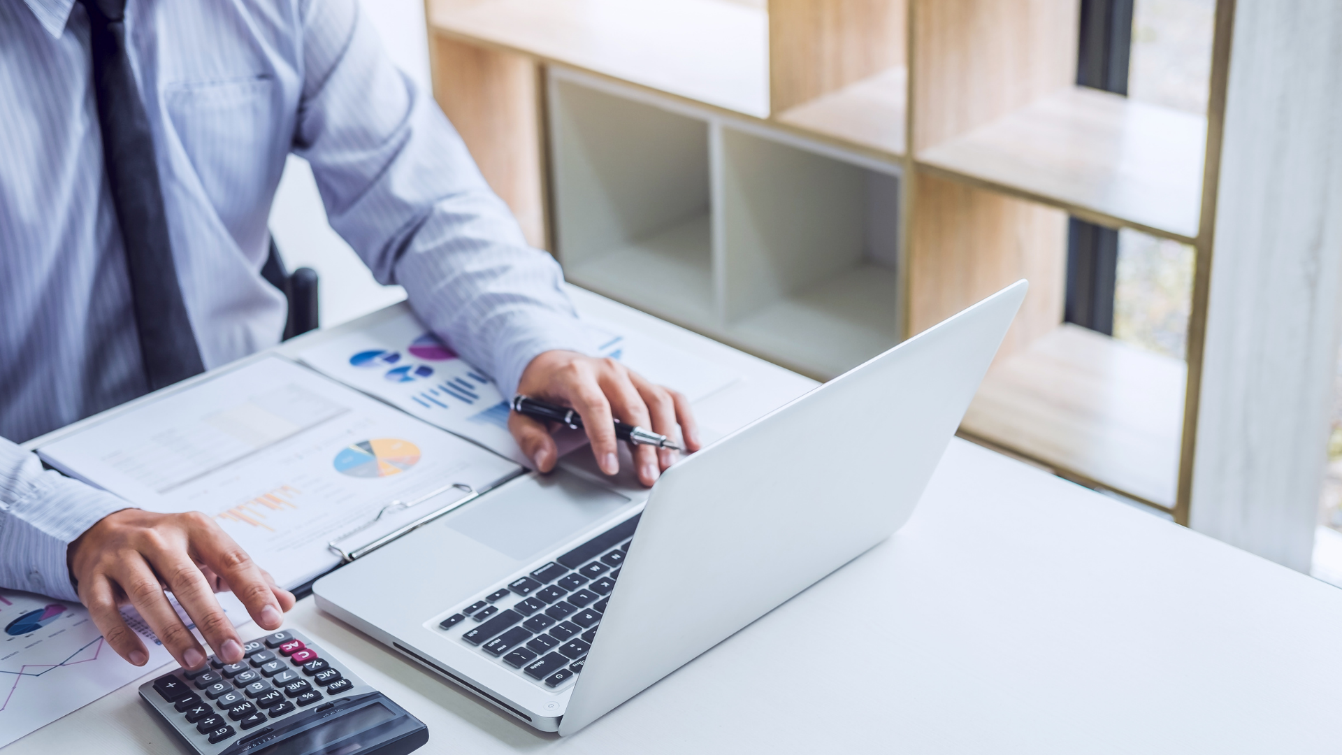 A man is sitting at a desk using a laptop and a calculator.