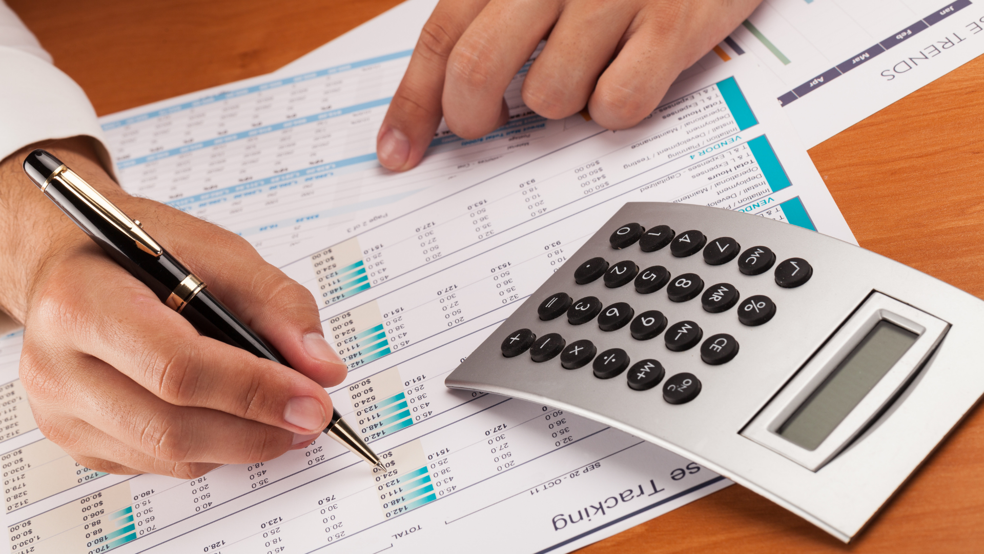 A person is writing on a piece of paper next to a calculator.