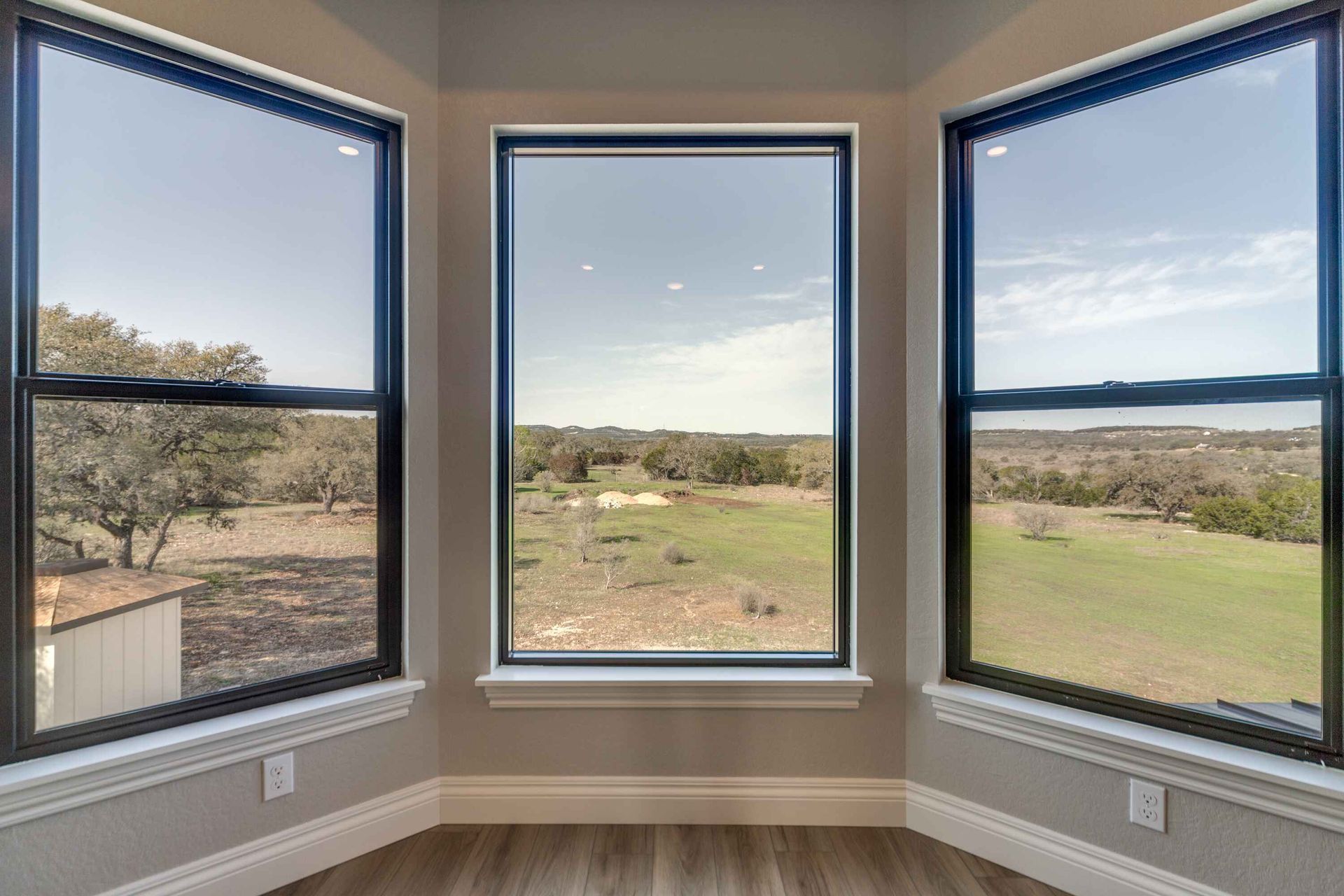 A room with three windows and a view of a field.
