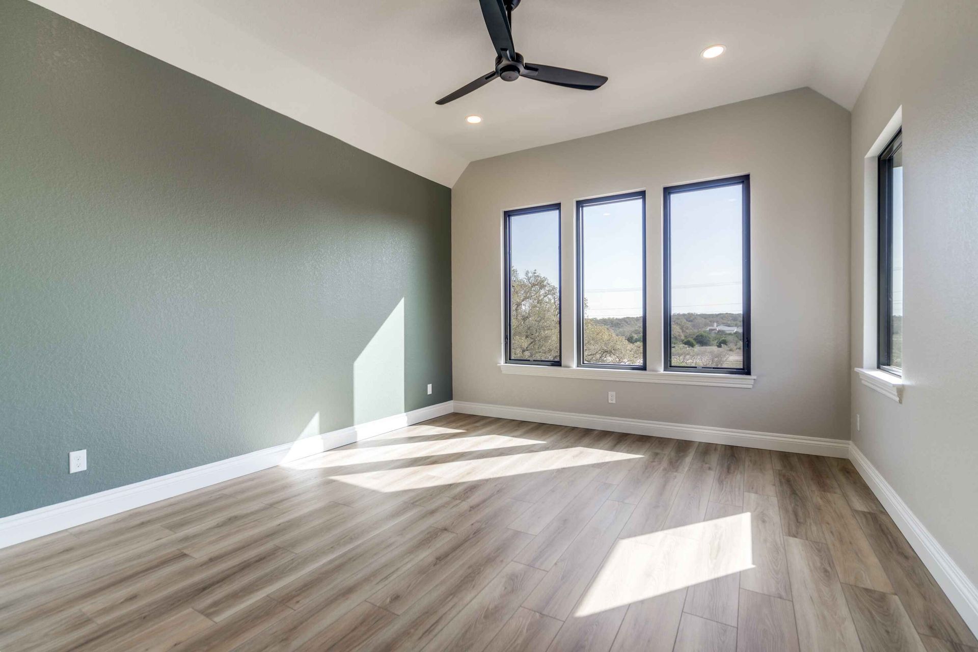 An empty room with a ceiling fan and three windows.