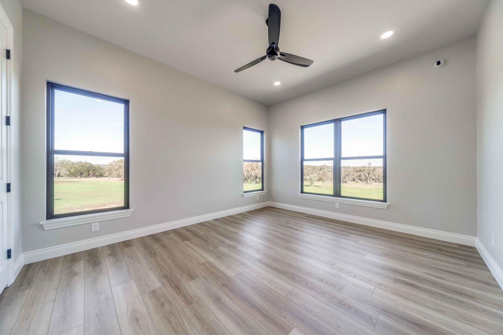 A large empty room with hardwood floors and a ceiling fan.
