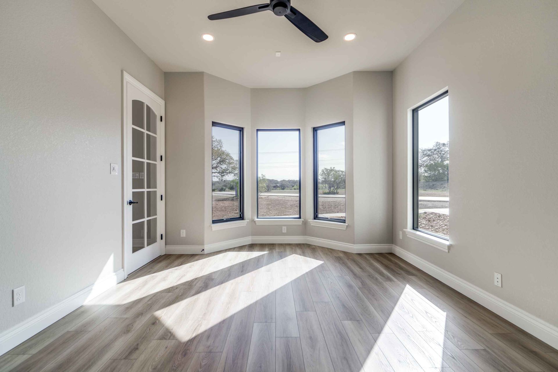 An empty room with a ceiling fan and three windows.