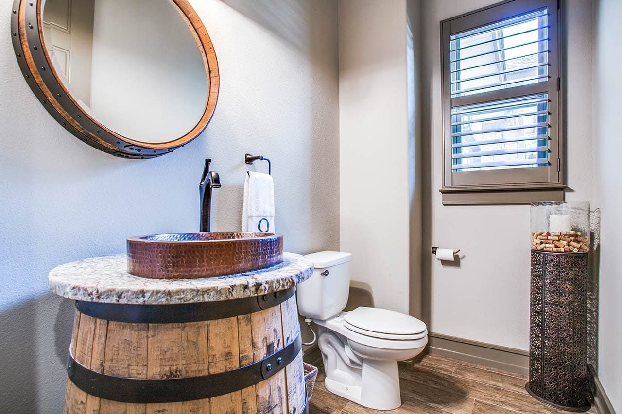 A bathroom with a toilet , sink and mirror . the sink is made out of a wooden barrel.