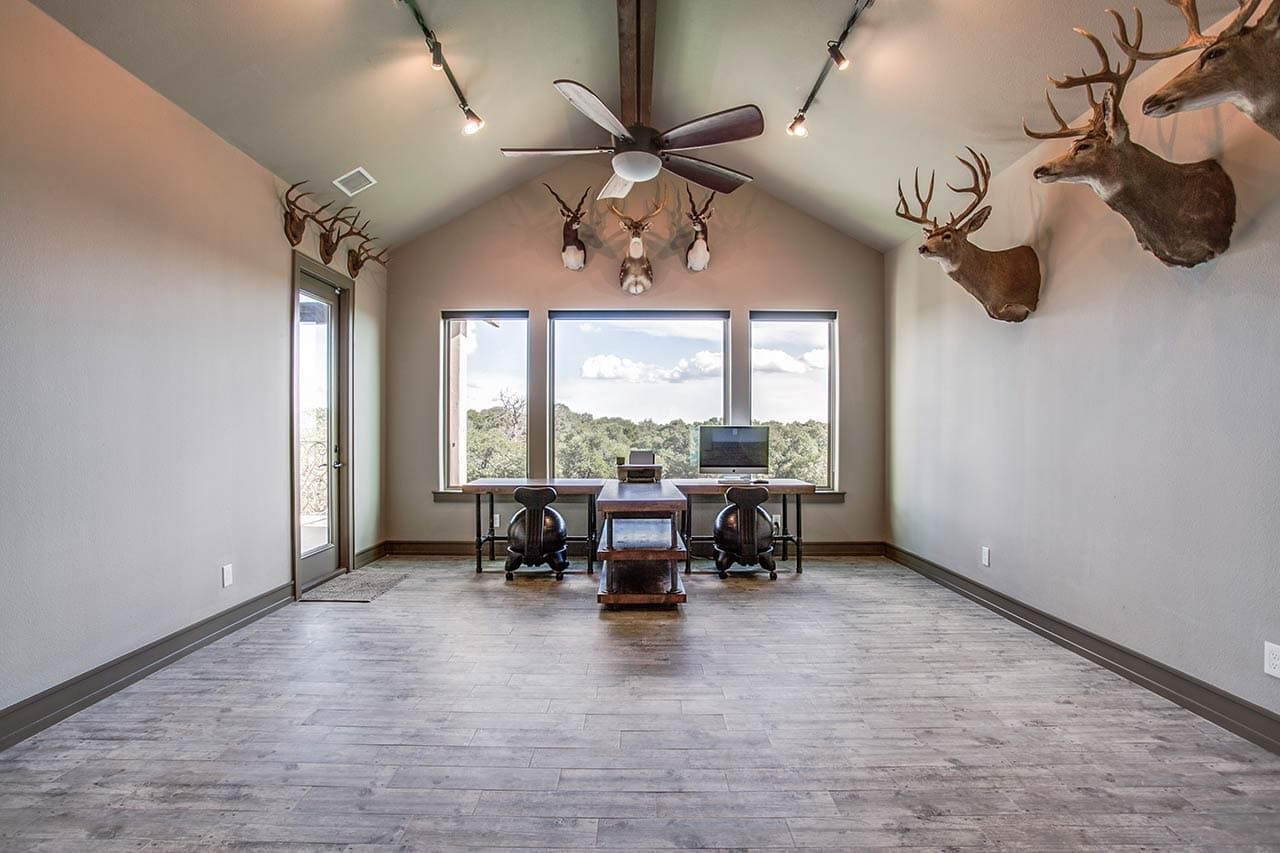 A large room with a desk , chairs , and a ceiling fan.