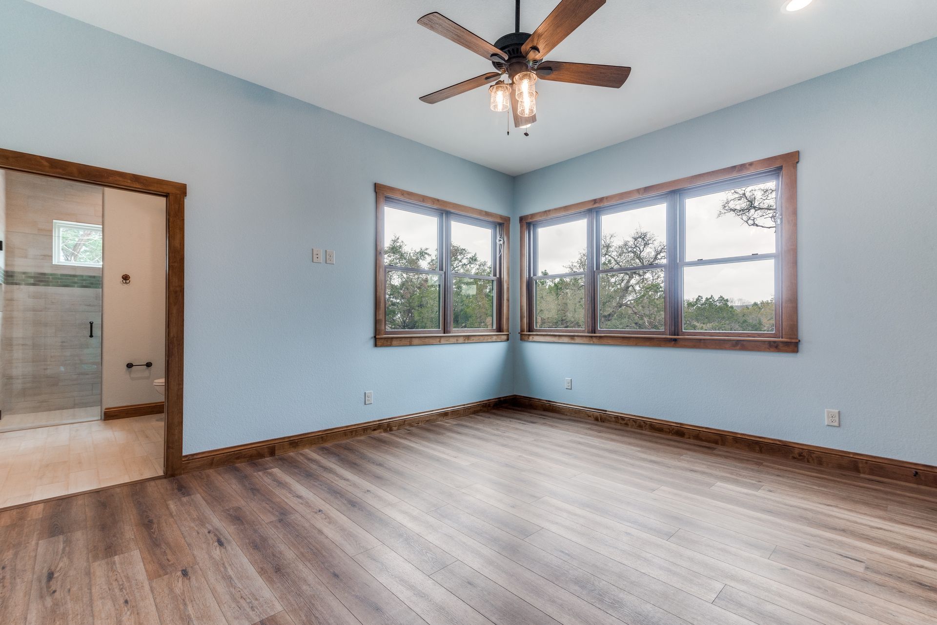 There is a ceiling fan in the room with a lot of windows.