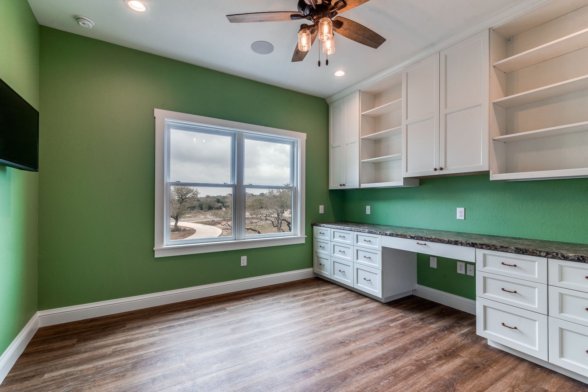 A room with green walls and white cabinets and a ceiling fan.