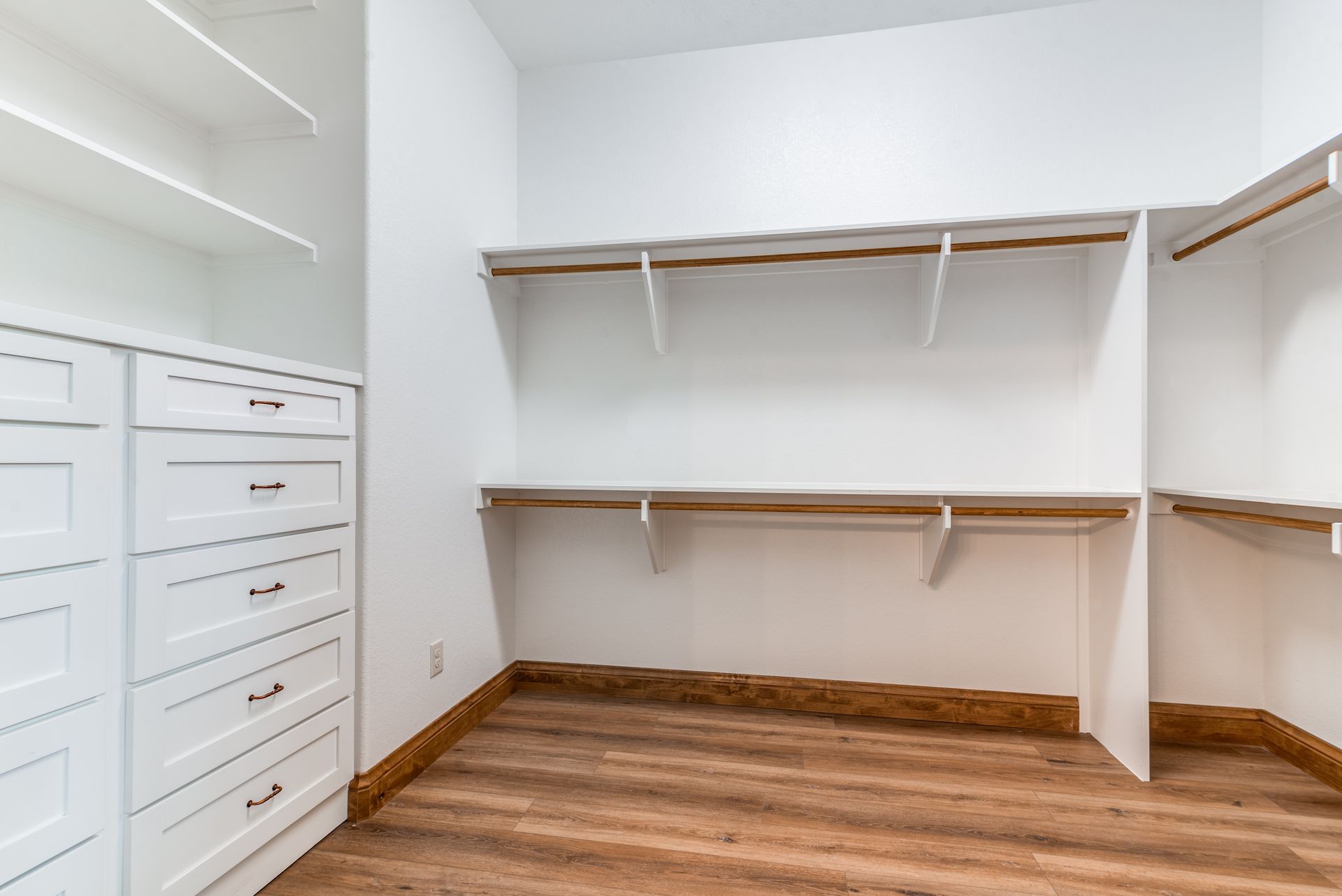 A walk in closet with white cabinets and wooden floors.