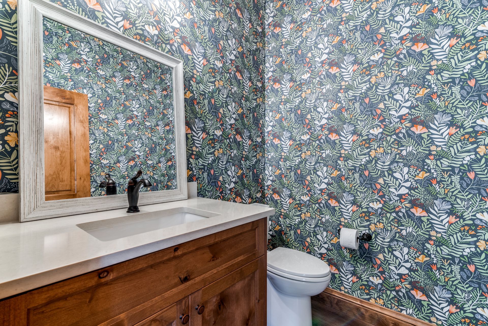 A bathroom with a sink , toilet , mirror and wallpaper.