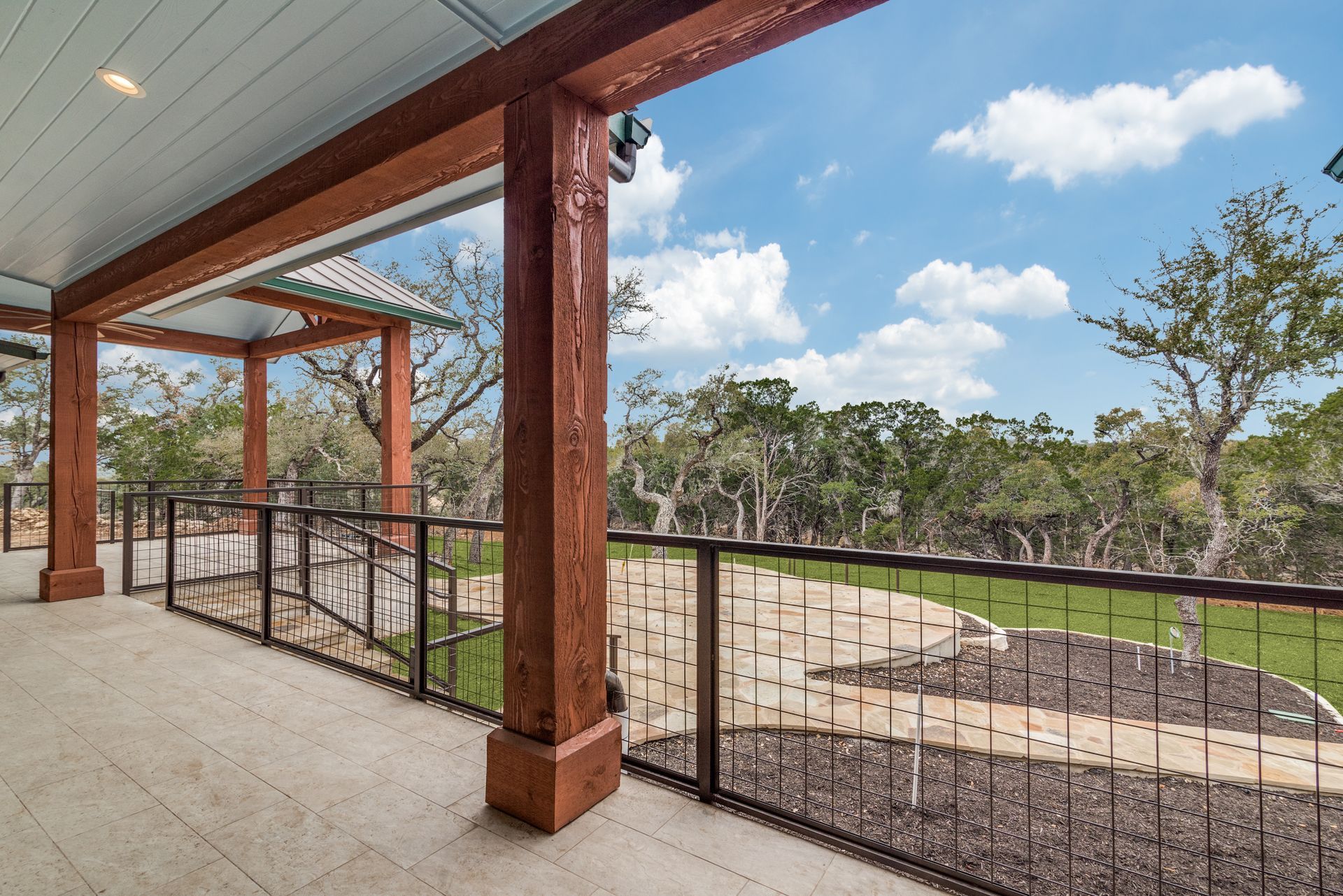 A large porch with a railing and a view of a lush green field.