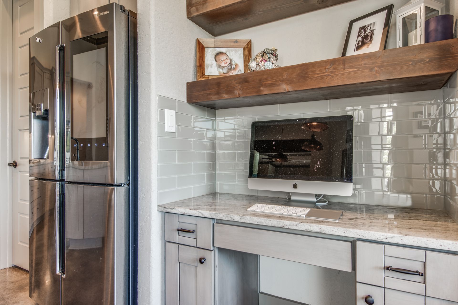 A kitchen with a refrigerator and a desk with a computer on it.