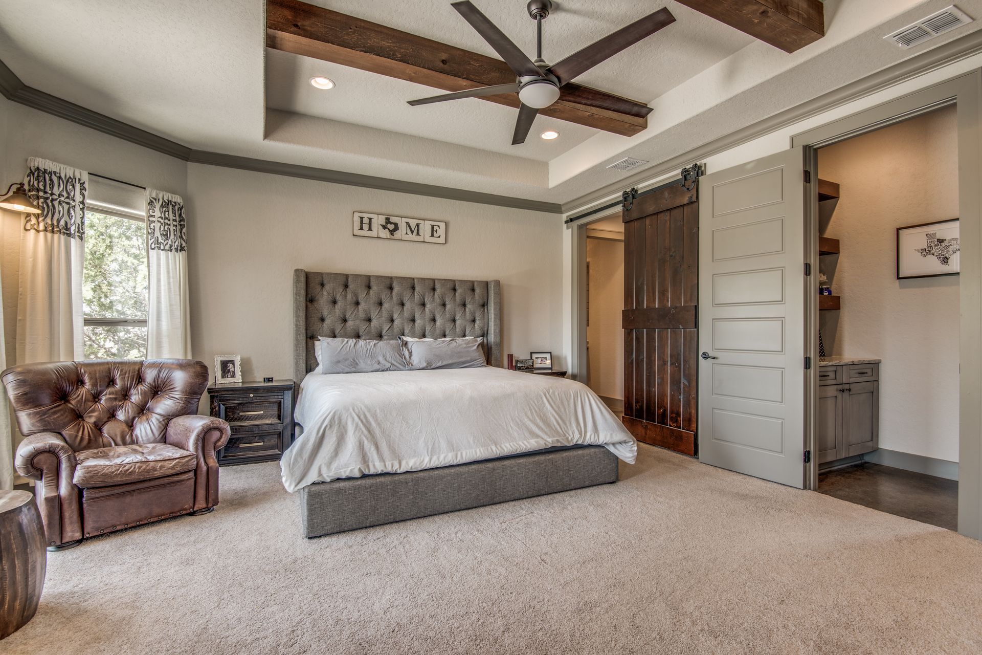 A large bedroom with a bed , chair , nightstand and ceiling fan.