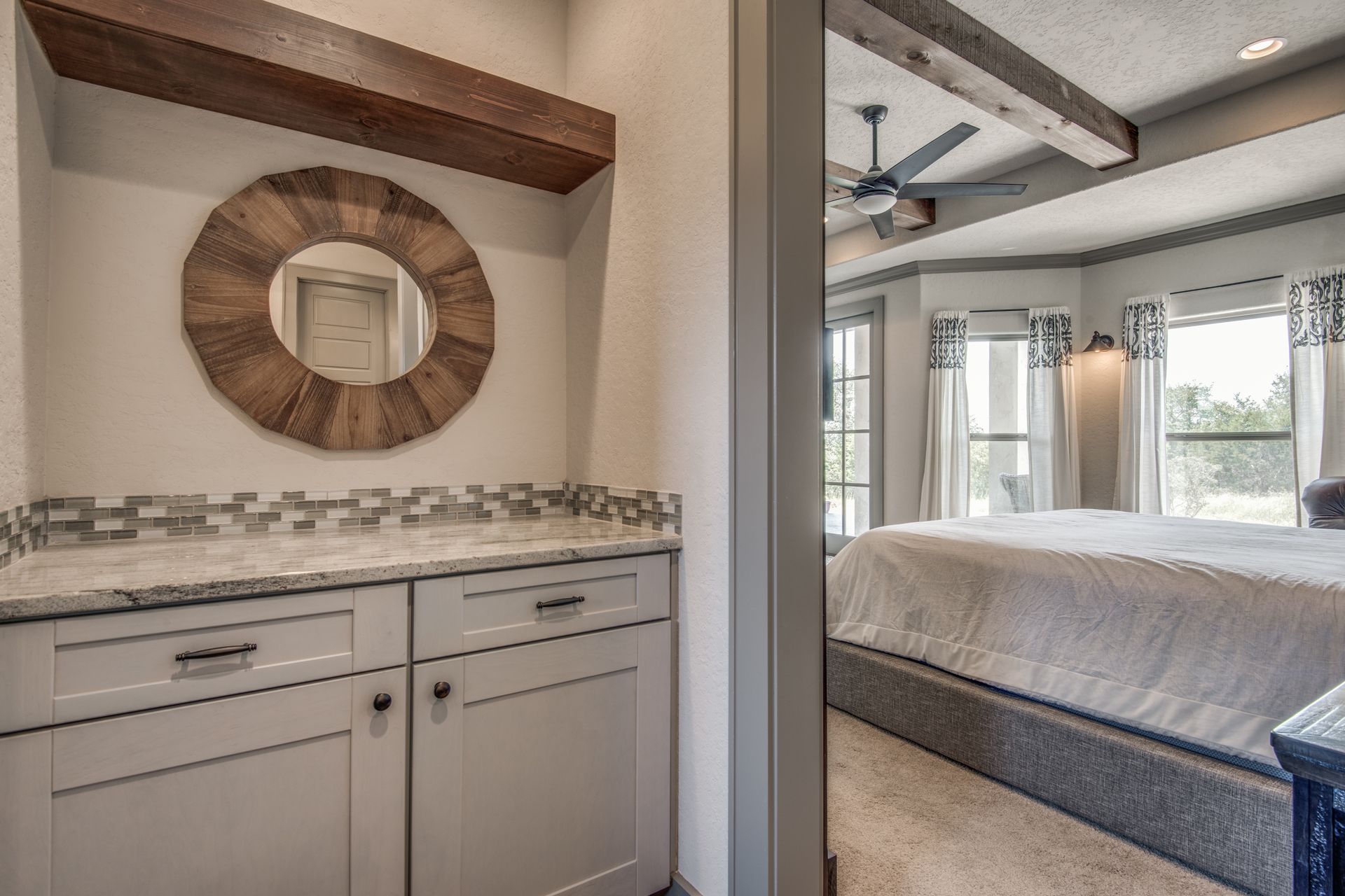 A bathroom with a sink and a mirror next to a bedroom with a bed.